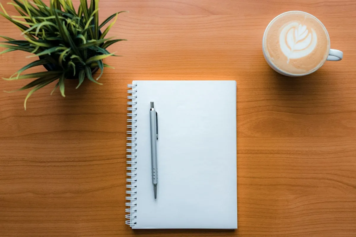 Overhead view of a notebook, pen and coffee on a wooden desk